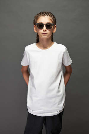 Kid girl wearing white t-shirt with space for your logo or design in studio over gray background with sunglassesの写真素材