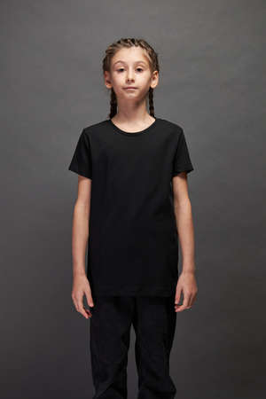 Kid girl wearing black t-shirt with space for your logo or design in studio over gray backgroundの写真素材