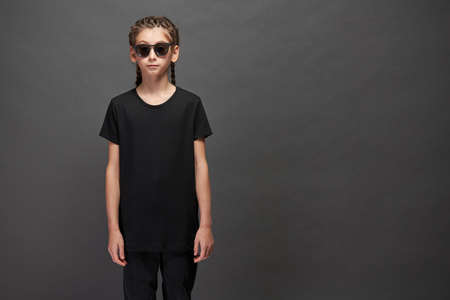 Kid girl wearing black t-shirt with space for your logo or design in studio over gray background with sunglassesの写真素材