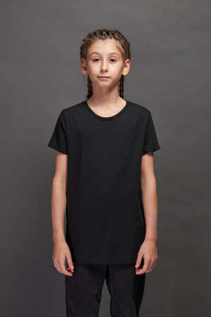 Kid girl wearing black t-shirt with space for your logo or design in studio over gray backgroundの写真素材