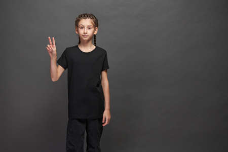 Kid girl wearing black t-shirt with space for your logo or design in studio over gray backgroundの写真素材
