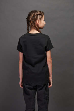 Kid girl wearing black t-shirt with space for your logo or design in studio over gray backgroundの写真素材