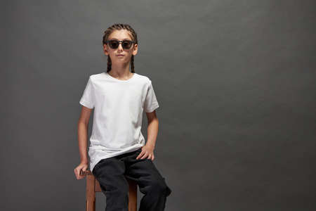 Kid girl wearing white t-shirt with space for your logo or design in studio over gray background with sunglassesの写真素材