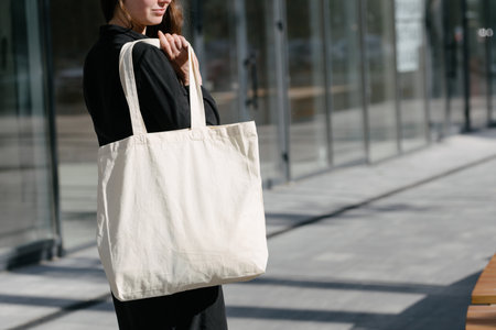 Woman holding white textile eco bag against urban city background. Ecology or environment protection concept. White eco bag for mock up.の写真素材