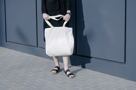 Woman holding white textile eco bag against urban city background. Ecology or environment protection concept. White eco bag for mock up.の写真素材
