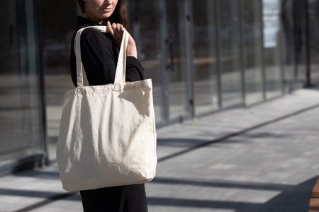 Woman holding white textile eco bag against urban city background. Ecology or environment protection concept. White eco bag for mock up.の写真素材