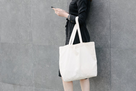 Woman holding white textile eco bag against urban city background. Ecology or environment protection concept. White eco bag for mock up.の写真素材