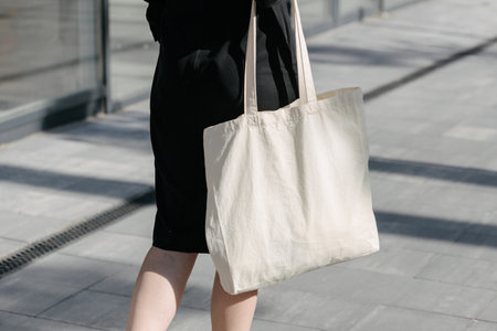 Woman holding white textile eco bag against urban city background. Ecology or environment protection concept. White eco bag for mock up.の写真素材