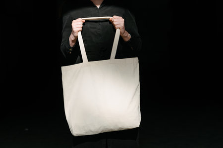 Woman holding white textile eco bag against urban city background. Ecology or environment protection concept. White eco bag for mock up.の写真素材