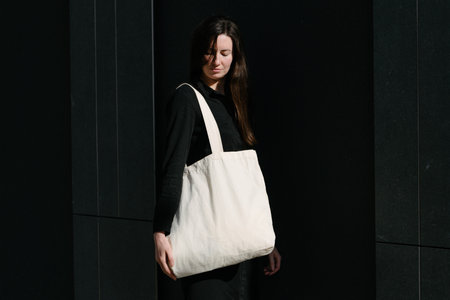 Woman holding white textile eco bag against urban city background. Ecology or environment protection concept. White eco bag for mock up.の写真素材
