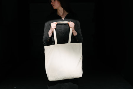 Woman holding white textile eco bag against urban city background. Ecology or environment protection concept. White eco bag for mock up.の写真素材