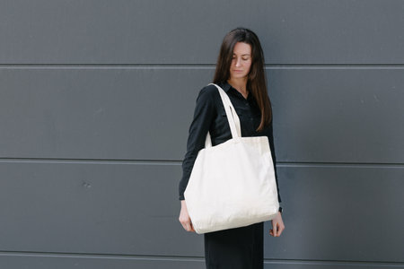 Woman holding white textile eco bag against urban city background. Ecology or environment protection concept. White eco bag for mock up.の写真素材