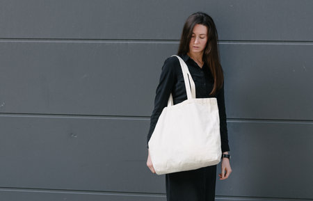 Woman holding white textile eco bag against urban city background. Ecology or environment protection concept. White eco bag for mock up.の写真素材