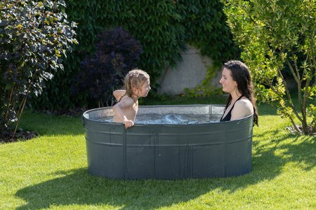 Mother having fun with a child in an outdoor bath tube in the backyard in summertimeの写真素材
