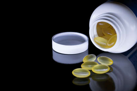 White jar with scattered yellow capsules of vitamins on a black isolated background