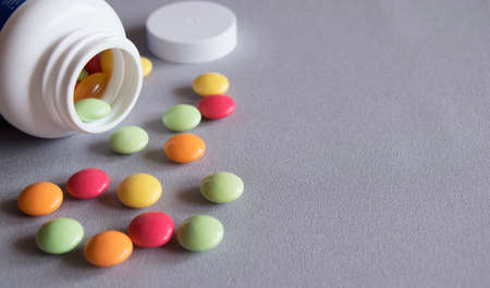 White jar with scattered multicolored of vitamins on a gray fabric close-upの写真素材