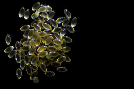 a bunch of yellow translucent vitamins capsules on a black background close-upの写真素材