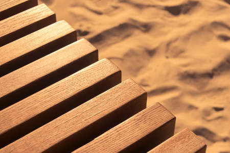 part of a wooden bench against a background of sand in the sunset lightの写真素材