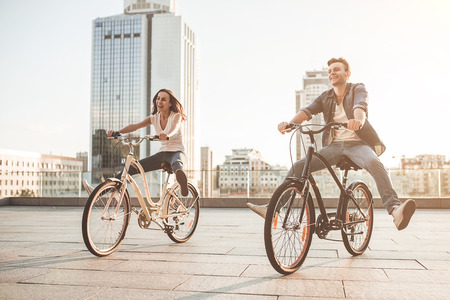Beautiful romantic couple is having fun in the city with bicycles on the sunset. Enjoying the company of each other.の写真素材