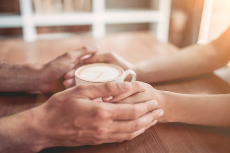 Side view of couple in love holding hands with coffee on wooden table.の写真素材