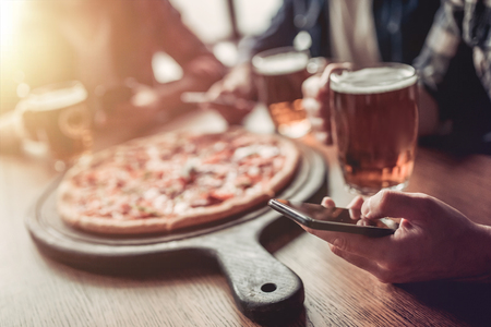 Cropped view of three male friends in bar drinking beer and eating pizza.の写真素材