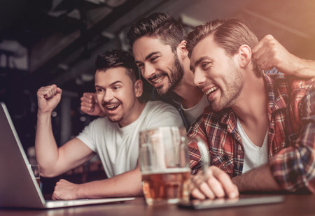 Happy excited fans are looking into the laptop, drinking beer and smiling.の写真素材