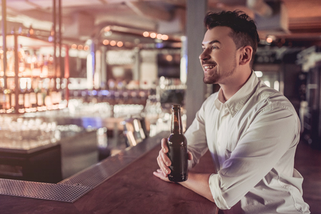 Handsome businessman in bar is drinking beer from bottle on bar counter and smilingの写真素材