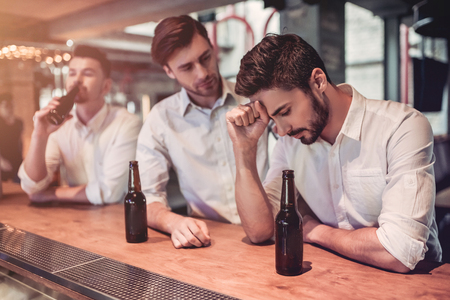 Young handsome businessmen in bar are drinking beer on a bar counter. Friends' support.の写真素材