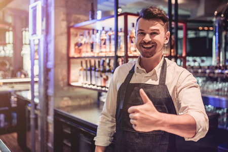 Cheerful bartender on a bar counter is working, smiling and showing thumb up.の写真素材