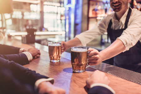 Cropped image of businessmen in bar are drinking beer. Cheerful bartender is smiling.の写真素材