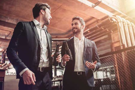 Successfull businessmen are drinking beer, communicating in bar and smiling. Discussing the latest news.の写真素材