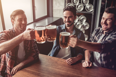 Cheers, my friends! Three handsome men are drinking beer, celebrating meeting and smiling.の写真素材