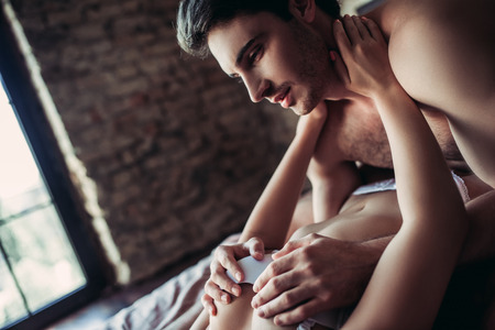 Beautiful passionate couple is having sex on bed. Man is holding woman's breast in hands.の写真素材