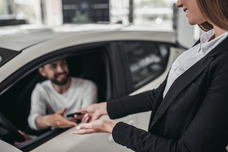 Professional salesperson during work with customer at car dealership. Giving keys to new car owner.の写真素材
