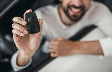 Cropped image of young man choosing a new vehicle in car dealership. Holding keys in hand and smiling.の写真素材
