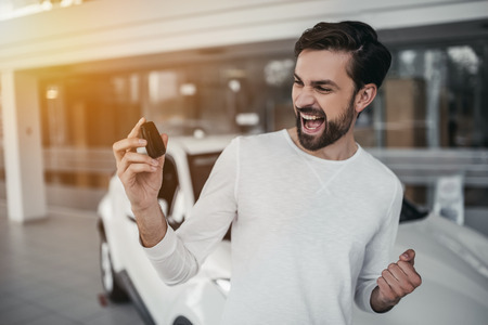 Young man is choosing a new vehicle in car dealership with keys in hand.の写真素材