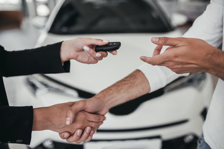 Professional salesperson during work with customer at car dealership. Shaking hands for successful deal and giving keys to new car owner.の写真素材