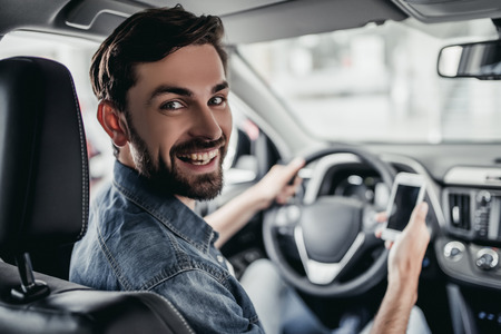 Young man is choosing a new vehicle at car dealership, smiling and looking at the camera.の写真素材
