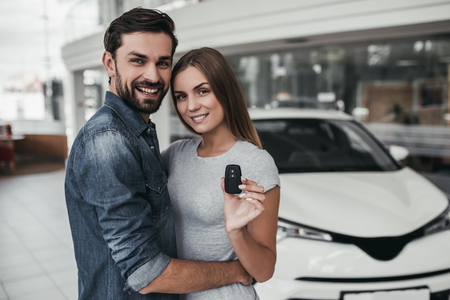 Happy beautiful couple is choosing a new car at dealership, smiling and looking at camera..の写真素材
