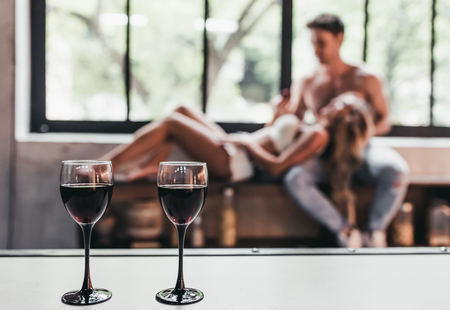Attractive passionate couple on kitchen. Two glasses of wine on the foreground.の写真素材