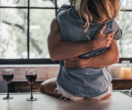 Cropped image of attractive passionate couple on kitchen. Man hugs woman while she's sitting on...