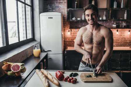 Sporty topless man is cooking on kitchen, looking at camera and smiling.の写真素材