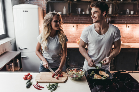 Attractive couple is cooking on kitchen. Looking on each other and smiling.の写真素材