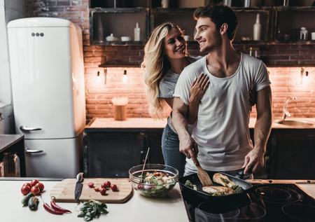 Attractive couple is cooking on kitchen. Looking on each other and smiling.の写真素材