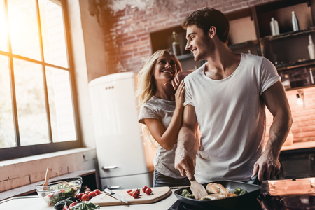 Attractive couple is cooking on kitchen. Looking on each other and smiling.の写真素材