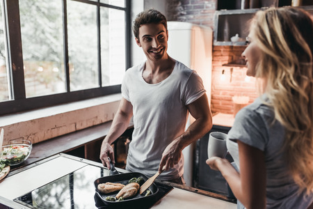 Attractive couple is cooking on kitchen. Looking on each other and smiling.の写真素材