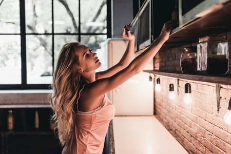 Attractive young woman is opening shelf on kitchenの写真素材