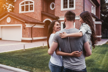 Back view of happy family is standing near their modern house and huggingの写真素材