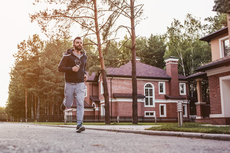 Handsome man in earphones is running outdoors near modern private houses.の写真素材