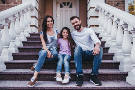 Happy family is sitting on porch of their modern private house, smiling and looking at camera.の写真素材